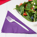 A plate of salad with strawberries, nuts, and a fork next to an amethyst Creative Converting luncheon napkin.
