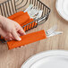 A hand holding a Sunkissed Orange luncheon napkin in a black metal basket.