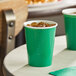 Two Creative Converting emerald green paper cups with ice and drinks on a table.