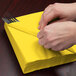 A person wrapping a School Bus Yellow Creative Converting luncheon napkin around a fork and knife.