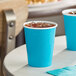 A turquoise blue Creative Converting paper cup filled with ice on a table.
