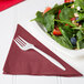 A plate of salad with strawberries, spinach, and a fork with a burgundy luncheon napkin on the side.