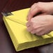 A person wrapping a Creative Converting Mimosa Yellow 3-ply luncheon napkin around a fork and spoon.