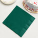 A hunter green Creative Converting 3-ply paper napkin with a slice of white cake on it.