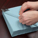 A person wrapping a Creative Converting Pastel Blue luncheon napkin around silverware.