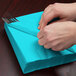 A person wrapping a Bermuda Blue Creative Converting luncheon napkin around a fork.