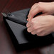 A person's hands wrapping silverware in a black velvet luncheon napkin.