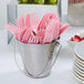 A bucket of pink forks on a table in an outdoor catering setup.