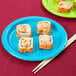 A turquoise blue paper plate with sushi and chopsticks on it.