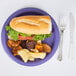 A purple paper plate with a sandwich and potato chips.