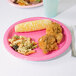 A Creative Converting candy pink paper plate on a table with food.