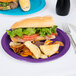 A sandwich and chips on a Creative Converting amethyst purple paper plate with a fork and knife.
