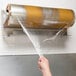 A hand using a Bulman stainless steel countertop film dispenser to wrap food with plastic film.