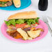 A sandwich and chips on a table with a Creative Converting Candy Pink paper plate.