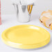 A stack of Creative Converting Mimosa Yellow paper plates next to a silver bucket of silverware.