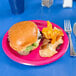 A hot magenta pink paper plate with a burger and chips on it.