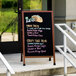 A cherry stained solid oak A-frame sidewalk board with a black porcelain marker board.