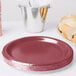 A stack of burgundy paper plates with a silver cup and food bucket.