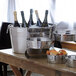 An American Metalcraft stainless steel round metal tub on a table filled with bottles of champagne.