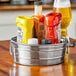 An American Metalcraft stainless steel round metal tub filled with condiments on a table.