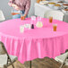 A woman sitting at a table with a pink Creative Converting plastic tablecloth and glasses of yellow liquid.