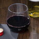 A WNA Comet clear plastic stemless wine goblet filled with red wine next to a bottle of wine.