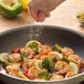 A hand sprinkles Regal Tangy Lemon Pepper Seasoning on shrimp and broccoli in a pan.