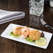 A Libbey rectangular porcelain plate with shrimp and lemon slices on a table.