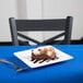 A Libbey white porcelain square plate with a piece of cake on a table with a silver spoon.