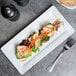 A Libbey white porcelain rectangular plate with a salad and vegetables on a table.