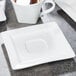 A Libbey white square porcelain saucer with a well ring on a table with a cup of tea.