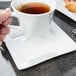 A person holding a white Libbey wide rim saucer with a cup of tea.