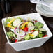 A Libbey ultra bright white square porcelain bowl filled with salad on a table in a salad bar.
