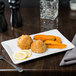 A Libbey white porcelain rectangular plate with food and a lemon slice on a table.