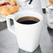 A white Libbey porcelain mug filled with brown liquid on a table.