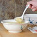 A hand using a Thunder Group Blue Bamboo soup ladle to pour soup into a bowl.