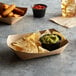 A Natural Eco-Kraft paper food tray with bowls of chips, guacamole, and red sauce on it.