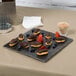 An American Metalcraft walnut melamine serving board with chocolate covered strawberries and chocolate covered eclairs on a table.