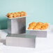 A stainless steel rectangular riser holding trays of pastries on a table.