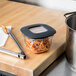 A Rubbermaid clear square food storage container with spaghetti inside on a cutting board.