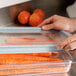 A person using a Cambro clear plastic lid to cover a container of carrots.