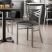 A metal cross back chair with a clear coat finish and a black vinyl padded seat.