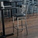 A Lancaster Table & Seating cross back bar stool with a black cushion on a table in a restaurant.