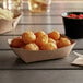 A pile of fried potatoes in a #25 Natural Eco-Kraft paper food tray on a table.