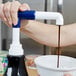 A person using a Ghirardelli sauce pump to pour brown liquid into a bowl.