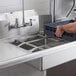 A man using a Regency slide bar to wash a blue container in a stainless steel sink.