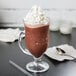A glass cup of Ghirardelli Chocolate Frappe Mix with whipped cream and a spoon.