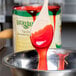A spoon with Lucky Leaf Strawberry Glaze on it over a bowl of red liquid.