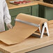 A person using a Bulman stainless steel paper cutter to cut brown paper on a counter.