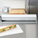 A sandwich wrapped in paper with lettuce and cheese on a cutting board.